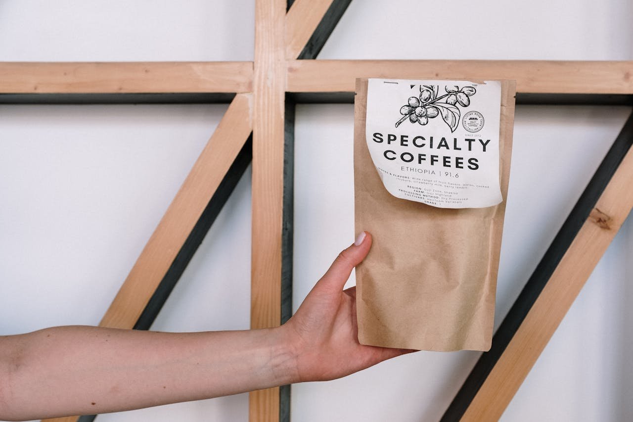 A hand holding a specialty coffee package against a minimalist background with wooden beams.